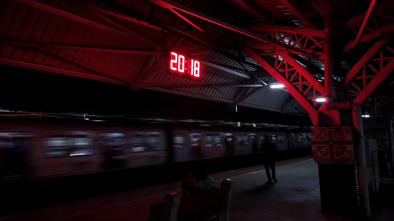 A glowing station clock above a passing Kolkata train at night