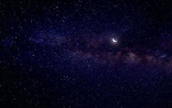 A small crescent moon glowing among countless stars at night